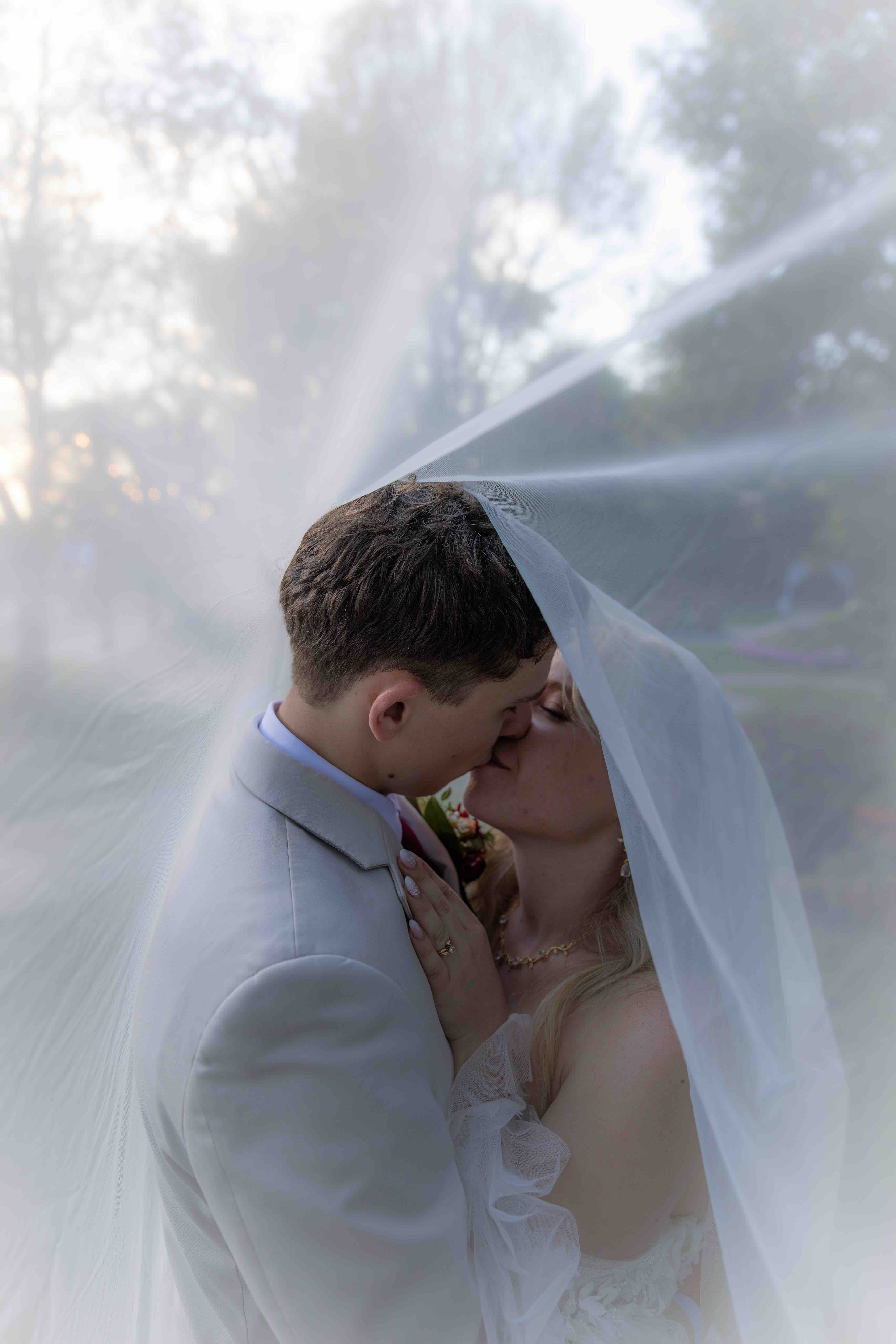 Bride and Groom under the veil kissing in romantic wedding photo